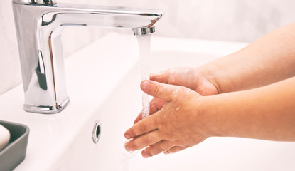 The boy is washing his hands with soap under the water