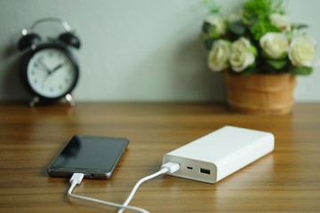 Smartphone is charging with backup battery or Power bank on the desk wooden table