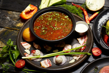 Borsch with sour cream, onions and a bun on a dark background
