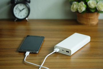 Fototapeta premium Smartphone is charging with backup battery or Power bank on the desk wooden table