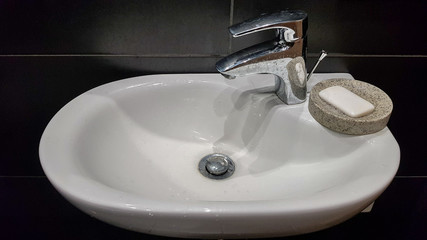 Bathroom interior with sink and faucet. Modern apartment in the attic of the house. White ceramic washbasin with chrome tap on a black tile wall