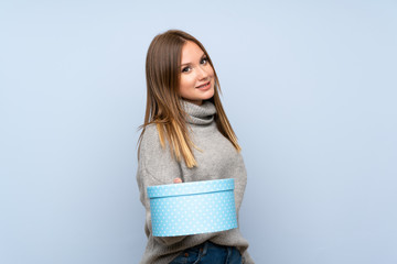 Fototapeta premium Teenager girl with sweater over isolated blue background holding gift box