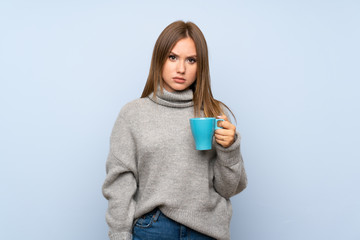 Teenager girl with sweater over isolated blue background holding hot cup of coffee