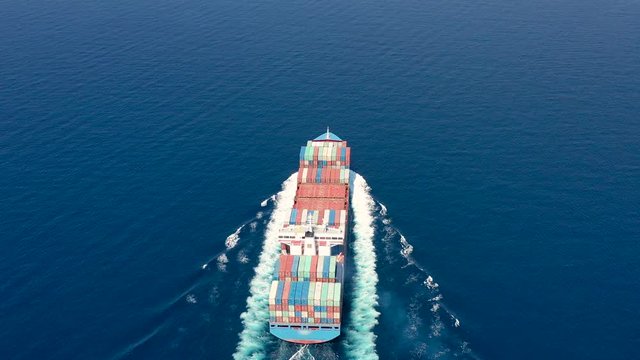 Luftaufnahme eines mit Containern beladenem Frachters in voller Fahrt &uuml;ber blauem Ozean