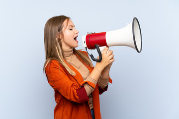 Naklejka premium Teenager girl with coat over isolated blue background shouting through a megaphone