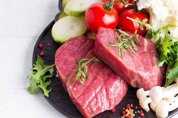 Raw beef steak on the bone with fresh vegetables in a pan on a marble background, top view