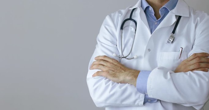 doctor in white coat standing with arms crossed on gray background. copy space