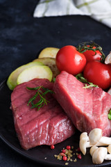 Raw beef steak on the bone with fresh vegetables in a pan on a dark stone background,