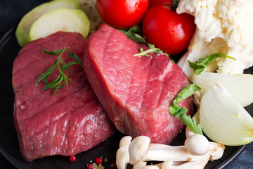 Raw beef steak on the bone with fresh vegetables in a pan on a dark stone background,