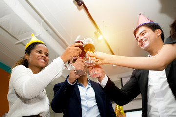 Group of happy colleagues having fun at a new year celebration ahead or business success. Coworkers with diverse ethnicities are toasting wine or champagne glasses at the office party.
