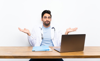 Young doctor man with his laptop over isolated wall having doubts with confuse face expression