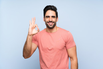 Naklejka premium Handsome young man in pink shirt over isolated blue background showing ok sign with fingers