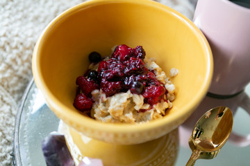 Old fashioned oats with simmered berries and black coffee on bed, breakfast in bed, copy space, cozy mornings