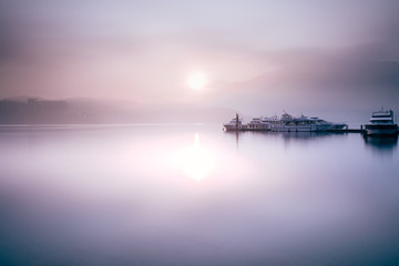 Beautiful tranquil landscape at Sun Moon lake in Nantao, Taiwan. Pier with boats and background of foggy mountains. Concept of peaceful, traanquility of nature.