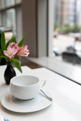 Empty white tea cup on table next to window with a view of the city, afternoon tea in high rise hotel