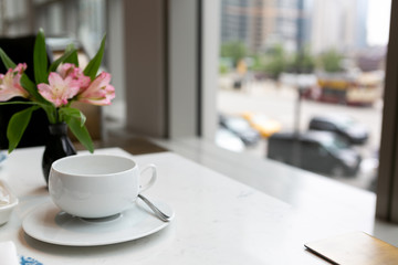 Empty white tea cup on table next to window with a view of the city, afternoon tea in high rise hotel
