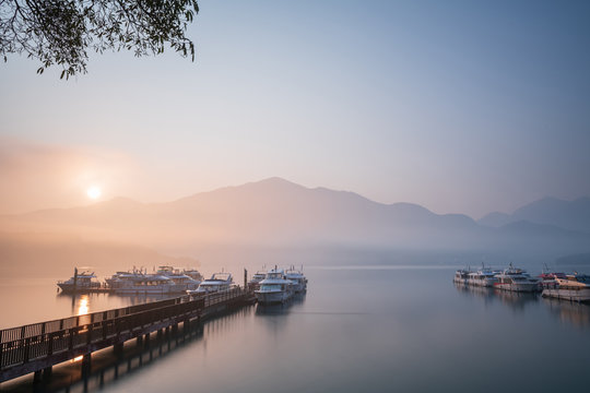 Beautiful tranquil landscape at Sun Moon lake in Nantao, Taiwan. Pier with boats and background of foggy mountains. Concept of peaceful, traanquility of nature.