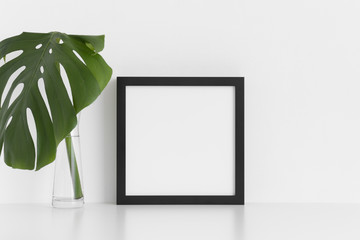 Black square frame mockup with a monstera leaf in a glass vase on a white table.
