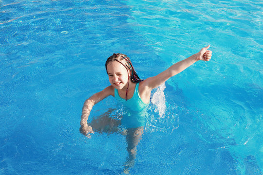 Happy cute girl in the pool on a sunny day shows like and winks