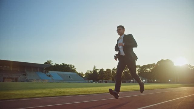 Young Serious Businessman in a Suit Running in an Outdoors Stadium. He Wears Glasses and is Holding a Mobile Phone. Office Worker Chasing Goals. Management Satire. Slow Motion Shot.