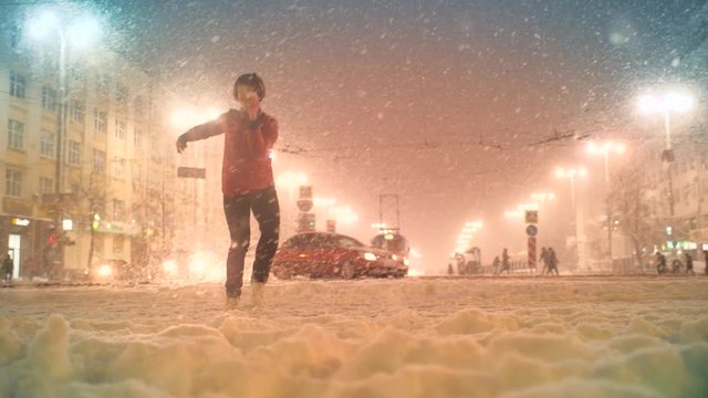 Beautiful happy young woman dancing in night city street intersection during winter snowfall