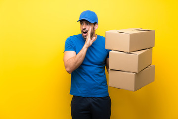 Young delivery man over isolated yellow wall whispering something