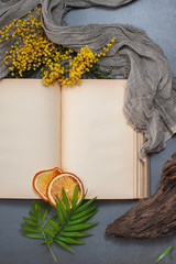 An open book with old blank pages, old cloth and floral decorations on a stone gray table.