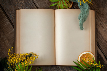 An open old book with blank pages and floral decor on an old wooden table.