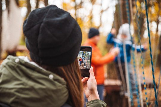 happy young family with toddler kid son playing at playground mother taking picture on phone