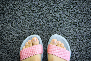 A woman wearing a pair of pink slippers on grey welcome mat texture background.