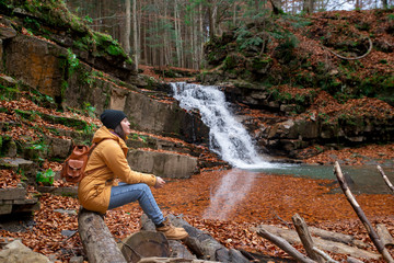 woman sitting on the log looking at waterfall autumn season