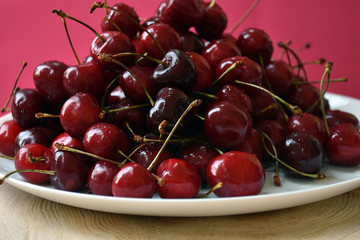 White bowl of fresh cherries on a wooden table on pink backgraund.