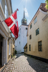 The danish flag hanging in a narrow alley with the church in the background