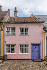 a small house in pink with a blue door on a cobblesone street