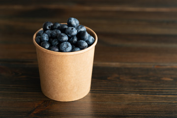 Fresh organic blueberries in a paper cup. Dark wooden table, high resolution