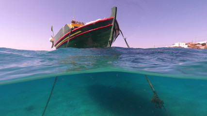 Above and below underwater photo of traditional fishing boat docked in turquoise  clear sea in port of Koufonisi island, Small Cyclades, Greece