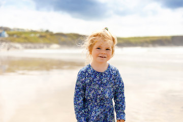 Little cute toddler girl at the Ballybunion surfer beach, having fun on surfboard for the first time, west coast of Ireland