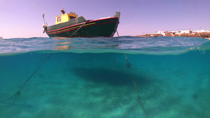 Above and below underwater photo of colourful fishing boat in turquoise clear Greek island sea