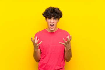 Young man over isolated yellow wall unhappy and frustrated with something