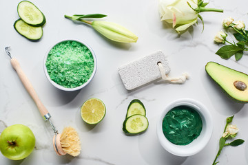 top view of natural clay mask, brush, pumice stone near apple, lime, cucumber, avocado and flowers...