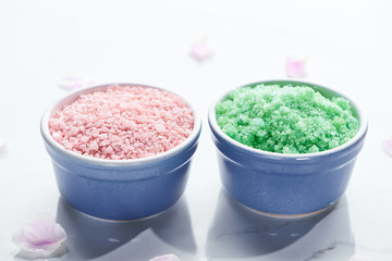 close up view of blue cups with bath salts on white surface with pink petals