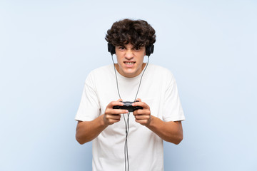 Young man playing with a video game controller over isolated blue wall