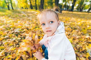 little smiling blond cute toddler girl at autumn city park