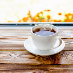 A white cup of tea stands on a wooden window sill next to books in the background of the window