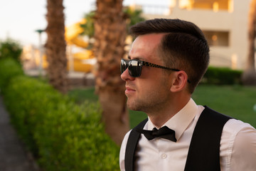 Side view portrait of the attractive young man in white shirt and sunglasses, blurred background