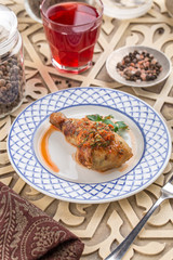 Grilled chicken legs with parsley on white plate and glass of red drink on oriental wooden table