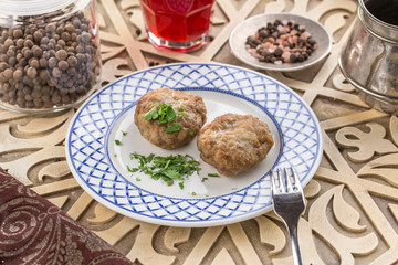 Meat patties on white plate with glass of red drink on oriental wooden table