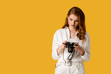 beautiful redhead girl holding digital camera isolated on orange