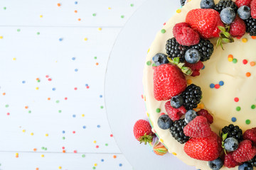 Cake on birthday with colorful rainbow cream on a white background decorated with berries, colorful sprinkles, poured with chocolate. Top view.