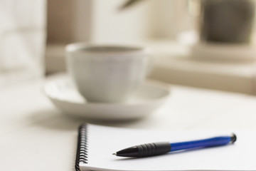 a clean notebook with a pen and a coffee Cup on the table by the window